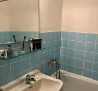 A bathroom with blue tiles, a sink, a bathtub, and a mirror in a studio apartment.