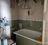 A bathroom in a 2-room apartment with a bathtub, tiles, and a clothes rack.