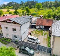A family house in Dúbravica surrounded by greenery with parking and neighboring buildings.