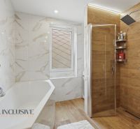A bathroom in a family house with a bathtub, a shower corner, and a floor with a wooden decor.
