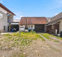 The courtyard of a family house in Dúbravica with farm buildings and a dog on the property.