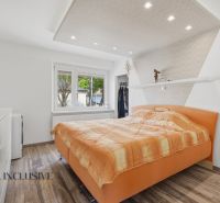 A bedroom with an orange bed, white furniture, and a wood-patterned floor in a family house.