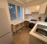 A kitchen in a studio apartment with a breakfast bar and a wooden decor floor.
