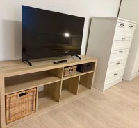 TV on a shelf with baskets, next to a dresser and a wardrobe, floor with wooden decor.