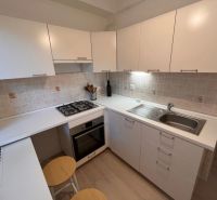 A kitchen with white cabinets, a built-in oven, and counter stools in a studio apartment.
