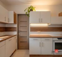 A kitchen with a wood-patterned floor, white and brown cabinets, a plant on the cabinet.