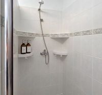 A shower corner in a 4-room apartment with light tiles and corner shelves.