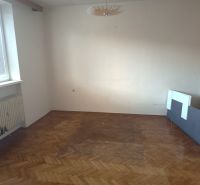 An empty room with a radiator and a wooden-patterned floor in a family house.