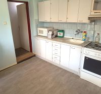 A kitchen with white cabinets, a microwave, and a wooden decor floor in a family house.