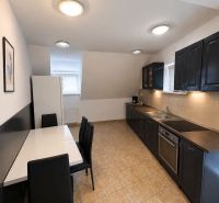 A kitchen in a 2-room apartment with black furniture and light ceramic flooring.