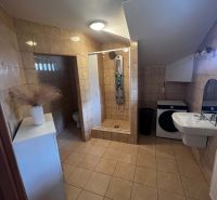 A bathroom in a 2-room apartment with a bathtub, sink, and washing machine, tiled with light tiles.