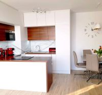 A kitchen with an island, white and wooden cabinets in a 3-room apartment with a wooden decor floor.