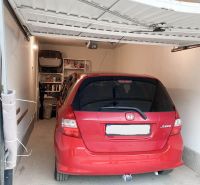 A red car parked in a garage with shelves on the wall, tiled floor.