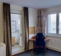 Room in a studio apartment with large windows, an office chair, and a desk.
