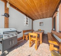 A terrace with a grill and wooden seating at a family house, wooden ceiling, bricks on the wall.