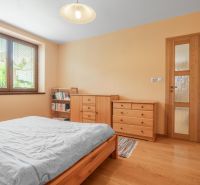A bedroom in a family house with a bed, dressers, and a floor with a wood decor.