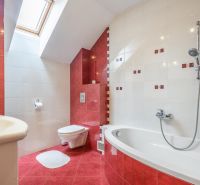 A bathroom in a family house with red and white ceramic tiles, a bathtub, and a window.