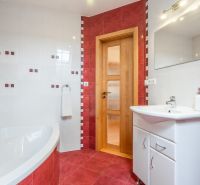A bathroom in a family house with white and red tiles and a corner bathtub.