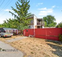 A family house in Bodza with a garden, a car, and a trailer by the road.