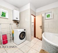 A bathroom in a family house with a washing machine, a corner bathtub, and a gas boiler.