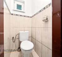 A small bathroom with a toilet, tiled with light tiles, with a window and a paper holder.