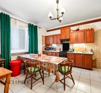 A kitchen in a family house with wooden cabinets, a dining table, and green curtains.