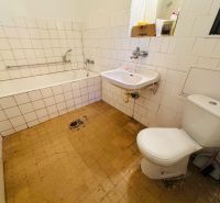 A bathroom in a 2-room apartment with a bathtub, sink, and toilet, tiled with white tiles.