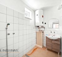 A bathroom in a family house with tiles, a shower, a boiler, and a sink with a wood-like finish.
