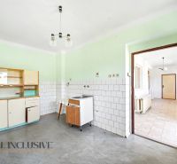 A kitchen in a family house with a simple kitchen unit, white tiles, and a gray floor.