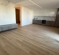 The kitchen area of a 3-room apartment with a wooden decor floor and white cabinets.