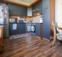 A kitchen in a 2-room apartment with a wood-patterned floor and dark furniture.