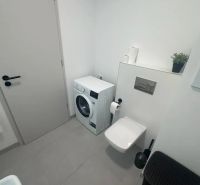 Bathroom with a washing machine, toilet, and beige tiles in a 2-room apartment.