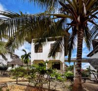 A family house in Pwani Mchangani surrounded by palm trees and flowers on a stone terrace.