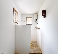 A bathroom in a family house with white walls, a shower corner, and windows.