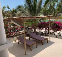 Wooden loungers on the sand with palm trees and flowers in a family house in Fumba Town.
