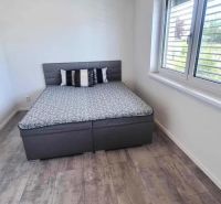 Bedroom with a bed, window, and wooden decor flooring in a family house.