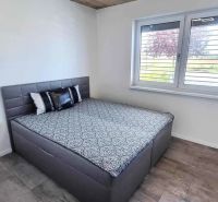 Family house with a bed and floor with wooden decor, simple concrete ceiling.