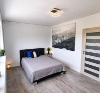 A bedroom in a family house with a large window, a bed, and a wooden decor floor.