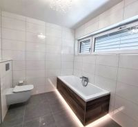 A bathroom in a family house with a wooden decor bathtub and a large window.