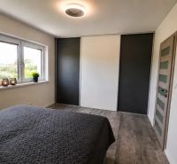 A bedroom in a family house with a large window and a bed, floor with wooden decor.