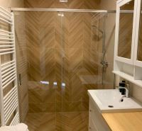 A bathroom with a shower and a floor with a wood decor in a 3-room apartment.