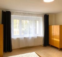 A bright bedroom with a large window and a wooden decor floor in a 3-room apartment.