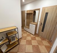 A hallway in a 3-room apartment with tiled flooring, a coat rack wall, and shelves with a wooden decor.