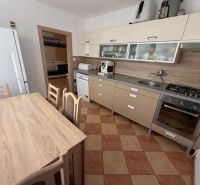 A kitchen of a 3-room apartment with a corner unit, dining table, and appliances.