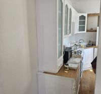 A kitchen in a family house with white furniture and a wooden-patterned floor.