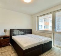 A bedroom in a 3-room apartment with a bed, a nightstand, and a floor with a wooden decor.
