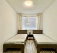 Two single beds, a nightstand, white walls, wood-patterned flooring.