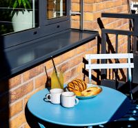 In the 2-room apartment, there is a blue table with cups and pastries on the balcony.