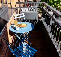 The balcony of a 2-room apartment with a blue table and chairs, wooden floor, reinforced railing.