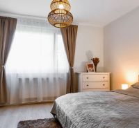 A bedroom in a 2-room apartment with decorative curtains and a wooden-patterned floor.